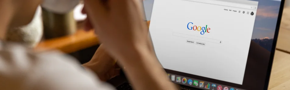 Persona en primer pla desenfocat mirant la pantalla d'una computadora portàtil oberta amb la pàgina d'inici del cercador de Google.