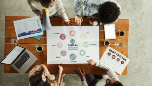 Vista aèria d'un equip de treball analitzant un esquema d'estratègies de màrqueting digital sobre una taula de fusta, amb documents d'anàlisi DAFO (SWOT) i ordinadors portàtils.