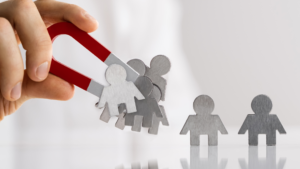Una mà que sosté un imant en forma de U de color vermell i atrau figures metàl·liques de persones, representant l'atracció de leads.