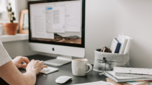 Persona trabajando en un escritorio de oficina con ordenador Mac, teclado, ratón, taza de café y libretas, representando la automatización de marketing B2B.