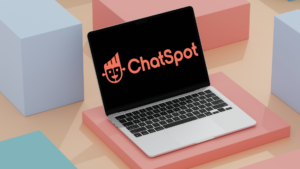 Laptop mostrant el logo de ChatSpot de HubSpot sobre un fons minimalista de blocs geomètrics en tons pastel.